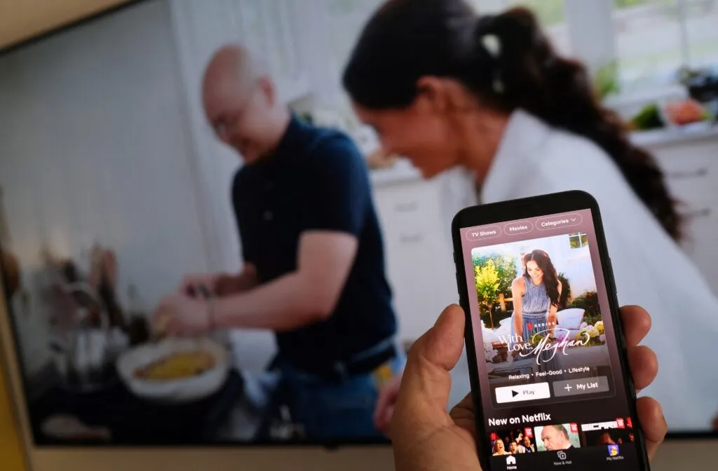 A phone shows Netflix’s Meghan Markle series while a TV plays footage of the show — the commercial route they pursued after leaving Britain.
